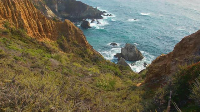 Slow zoom down a steep slope into the Blue Pacific Ocean waters at Big Sur