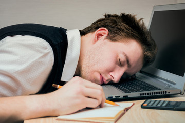 A sleeping young man on a laptop at work