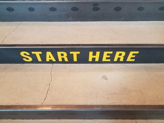 yellow start here sign on black and grey cement stairs