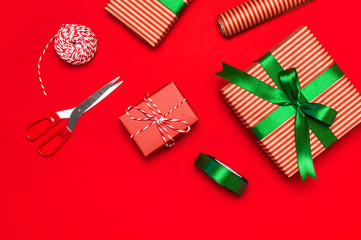 Gift boxes, packing paper, scissors, ribbon on red background. Festive background, congratulation, gift wrapping, Christmas and new year theme. Flat lay, top view, copy space.
