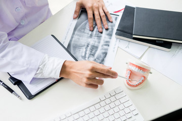 Concentrated dentist sitting at table with jaw samples tooth model in dental office professional dental clinic