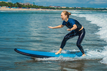 Joyful young woman beginner surfer with blue surf has fun on small sea waves. Active family...