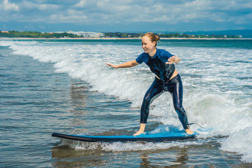 Joyful young woman beginner surfer with blue surf has fun on small sea waves. Active family...