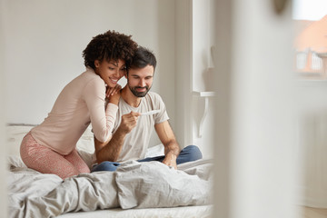 Parenthood, good news, baby expecting concept. Joyful dark skinned wife leans shoulder of her...