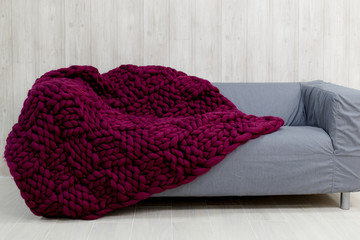 Purple merino wool blanket on grey sofa. Blanket of thick yarn. Chunky knit.