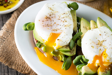 Avocado toast, cherry tomato on wooden background. Breakfast with toast avocado, vegetarian food, healthy diet concept. Healthy sandwich with avocado and poached eggs.