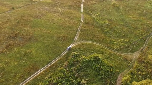White car on scenic unpaved road with fork aerial tracking shot on sunset