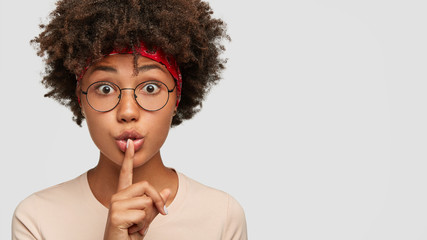 Photo of secret stupefied dark skinned woman makes silence gesture, afraids of gossiping, wears...