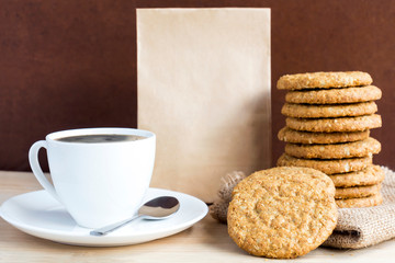Homemade shortbread cookies made of oatmeal stacked on sackcloth with paper bag and coffee cup on wooden table background. Concept food healthy snack for enjoy in holiday with copy space for text.