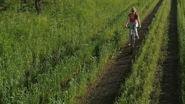 Cute young girl on bicycle in green field at summer, drone shooting