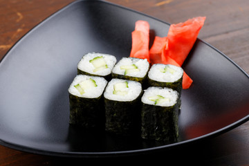 Vegetarian sushi with cucumber. Set sushi rolls with ginger on a black plate on a dark wooden background.