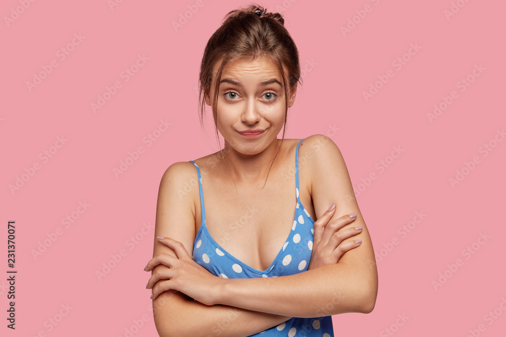 Wall mural horizontal shot of clueless woman keeps hands crossed over chest, has indecisive clueless expression - Wall murals