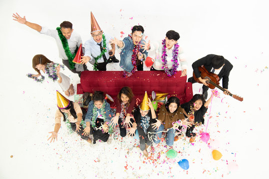 Top view, Group of cheerful joyful Asia young people standing and sitting celebrating together around red sofa with balloon in white background, new year party concept.