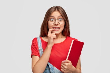 Pretty student looks with curious expression, eyes full of interest, surprisement, bites fore...