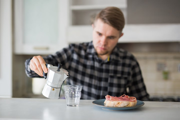 People, breakfast and drinks concept - handsome bearded young man is drinking coffee in kitchen