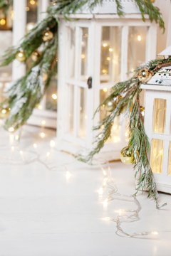 Christmas lanterns and snowy fir branches over white wooden background with lights.  New Year's decoration with a fir tree in white tones.