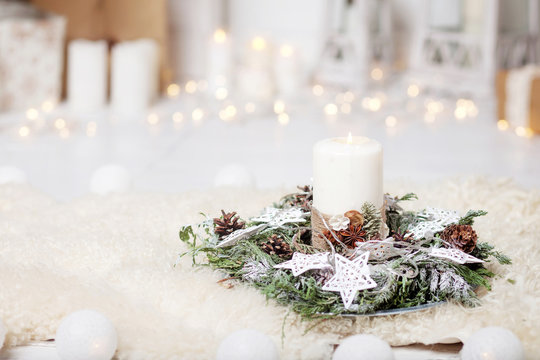 Christmas candles and snowy fir branches over white wooden background with lights.  New Year's decoration with a fir tree in white tones.
