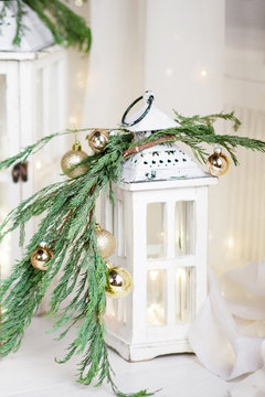 Christmas  lantern over white wooden background with lights.  New Year's decoration with  fir branches in white tones.