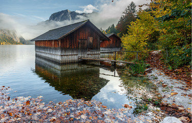 Beautiful landscape of alpine lake, with crystal clear water. Amazing Foggy Landscape on Altaussee lake. Majestic Mountains in the Fog on Background. wooden huts in the Water with Colorful leaves