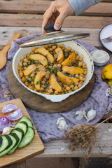 Woman hands open lid of baked chickpea with quince in cast iron skillet, frying pan. Vegan vegetarian lunch, paleo diet, healthy dinner served with salad and vegetables on table