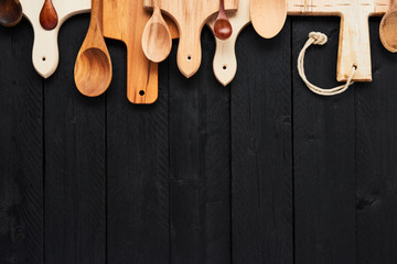Top view of assorted wooden spoons and chopping boards on black wooden table with copy space. Food background concept.