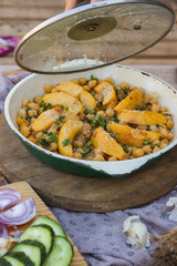 Woman hands open lid of baked chickpea with quince in cast iron skillet, frying pan. Vegan vegetarian lunch, paleo diet, healthy dinner served with salad and vegetables on table