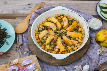 Baked chickpea with quince in cast iron skillet, frying pan with wooden spatula on it. Vegan vegetarian lunch, paleo diet, healthy dinner served with salad and vegetables on table. Top view