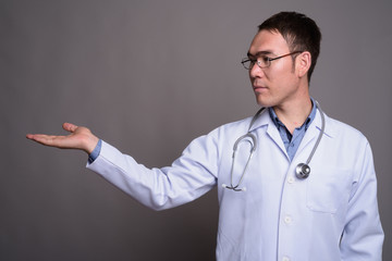 Young Asian man doctor against gray background