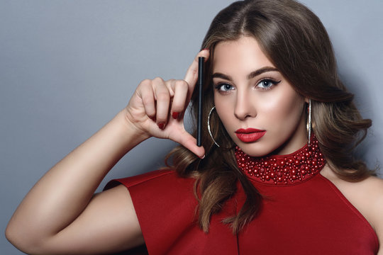 Close up portrait of young beautiful model with perfect make up and long wavy hair holing a black eyeliner at her face