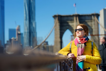 Obraz na płótnie Canvas Happy young woman tourist sightseeing at Brooklyn Bridge, New York City, at sunny spring day. Female traveler enjoying view of downtown Manhattan.
