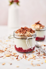 Healthy breakfast. Two jars of healthy yogurt with strawberry sauce, oat and chocolate on white marble table. Close up with copy space.