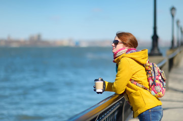 Happy young woman tourist sightseeing in New York City at sunny spring day. Female traveler drinking coffee in downtown Manhattan.