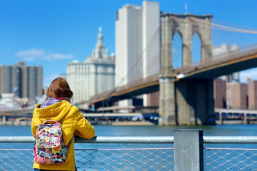 Happy young woman tourist sightseeing by Brooklyn Bridge, New York City, at sunny spring day....