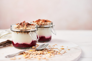 Healthy breakfast. Two jars of healthy yogurt with strawberry sauce, oat and chocolate on white marble serving plate over pink background with copy space.