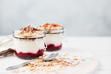 Healthy breakfast. Two jars of healthy yogurt with strawberry sauce, oat and chocolate on white marble serving plate over blue background with copy space.