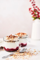 Healthy breakfast. Two jars of healthy yogurt with strawberry sauce, oat and chocolate on white marble serving plate over pink background with copy space.