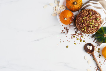 Top view of autumn whole wheat bread on white marble table with pumpkins, seeds, flax and wooden spoon on white marble table. Copy space.