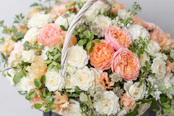 Wicker basket with mix beautiful flowers on wooden table near gray wall. Beautiful garden flowers in the arrangement , the work of a professional florist. European floral shop