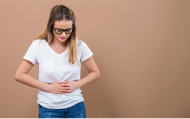 Young woman suffering from stomach pain on a brown background