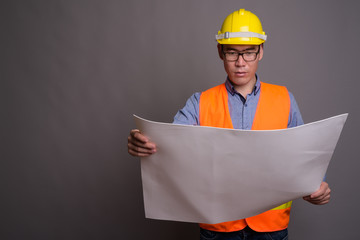 Young Asian man construction worker against gray background