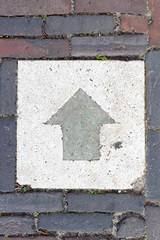Square concrete arrow sign on floor at the street with bricks around.