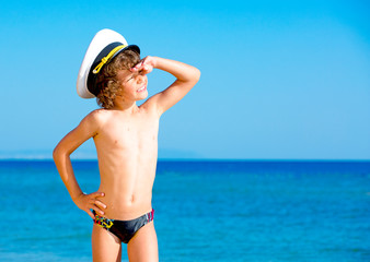 Funny child in black swimming trunks in a sea cap looking into the distance on the background of blue sea and sky