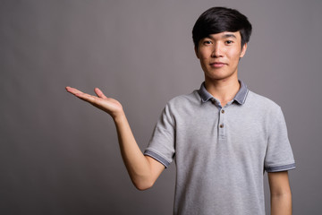Young Asian man wearing gray polo shirt against gray background