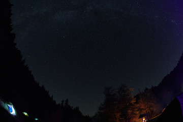 Naklejka premium campsite on a glade in a pine woods in fall at night. Night view of campsite and starry sky in mountains