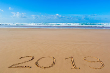2019 inscription written in the wet yellow beach sand