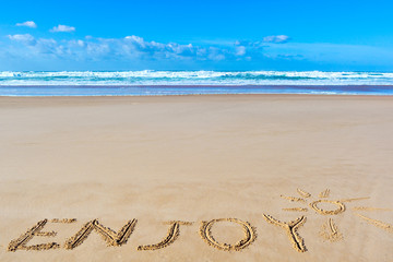 Fototapeta na wymiar Enjoy inscription on wet beach sand under the sun drawing and sea waves on background