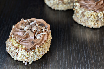 Biscuit cake sprinkled with nut crumb and decorated with chocolate cream are on a dark wooden desk