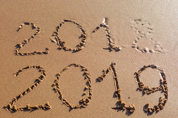 2018 2019 inscription written in the wet yellow beach sand being washed with sea water wave