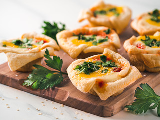 Ideas and recipes for healthy Vegan Shakshouka cups with vegan tofu eggs and turmeric yolk, on white marble table. Puff filo pastry,tomato and vegetable sauce, fresh green parsley. Copy space for text