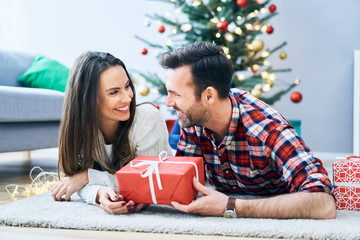 Cute couple relaxing in living room and exchanging christmas present